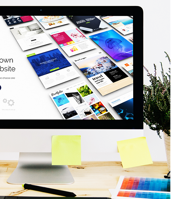Computer screen showcasing website designs, with sticky notes and design tools on a desk.