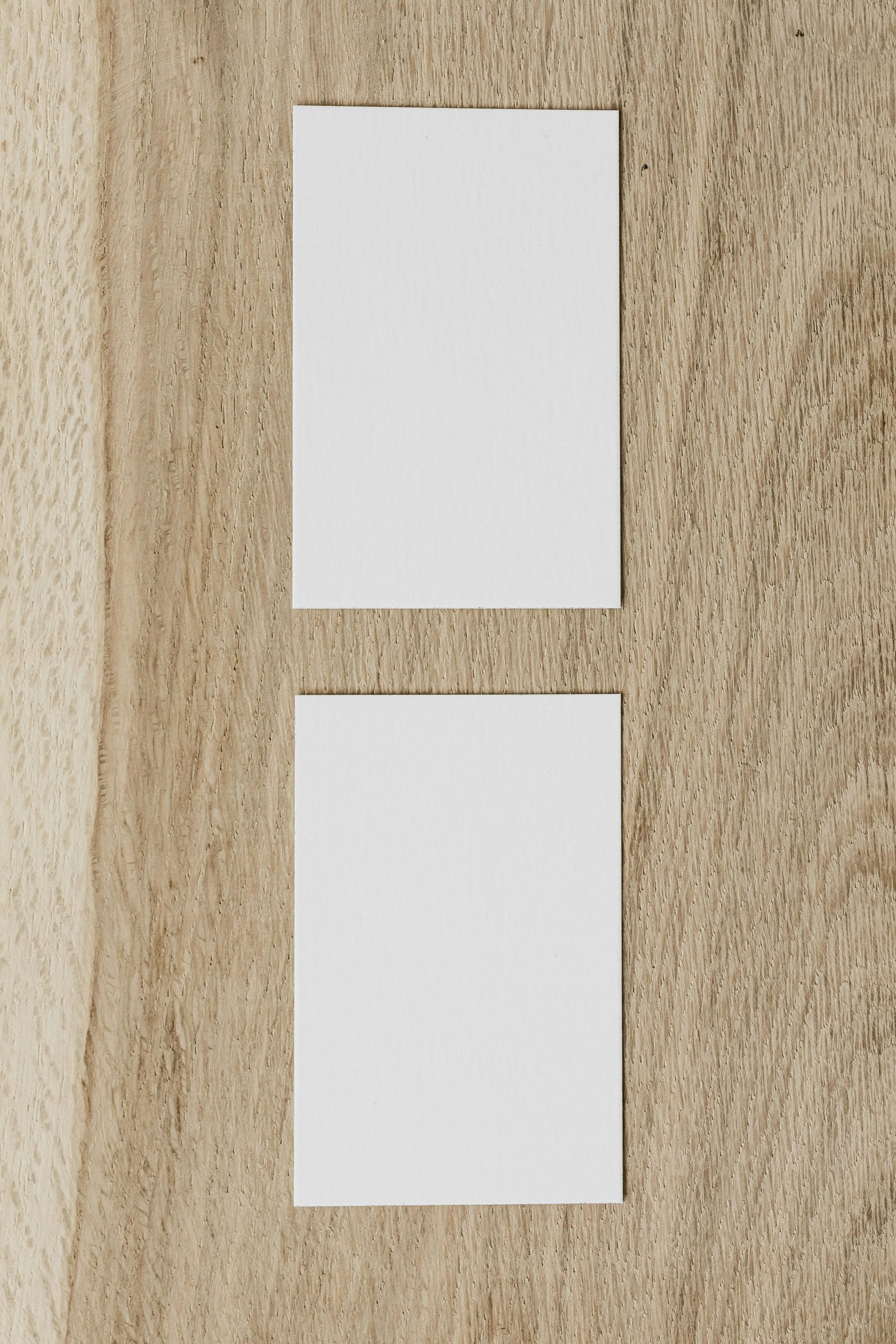 Two blank white cards on a textured, light brown wooden surface.