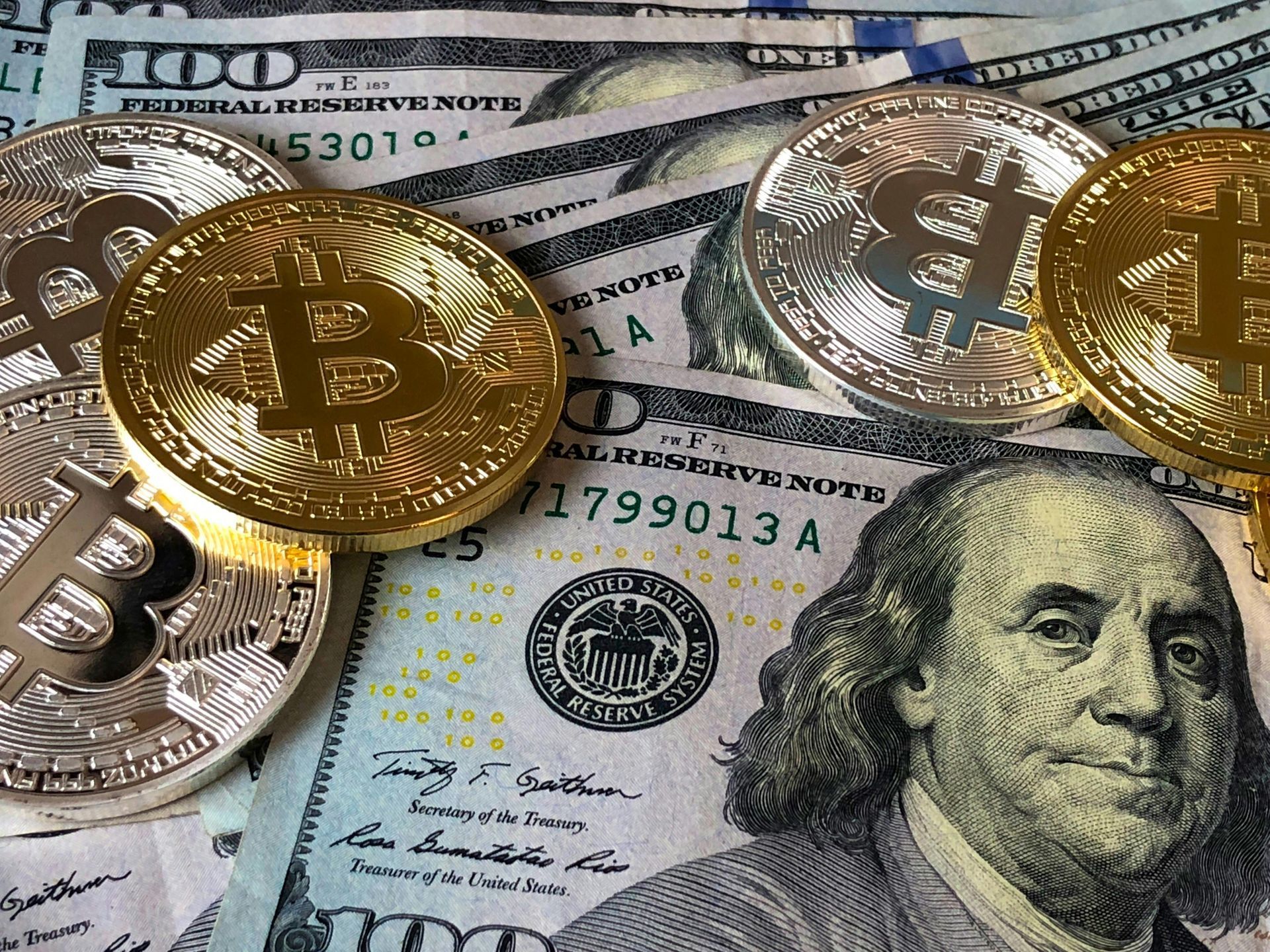 Bitcoin coins on top of US hundred dollar bills.