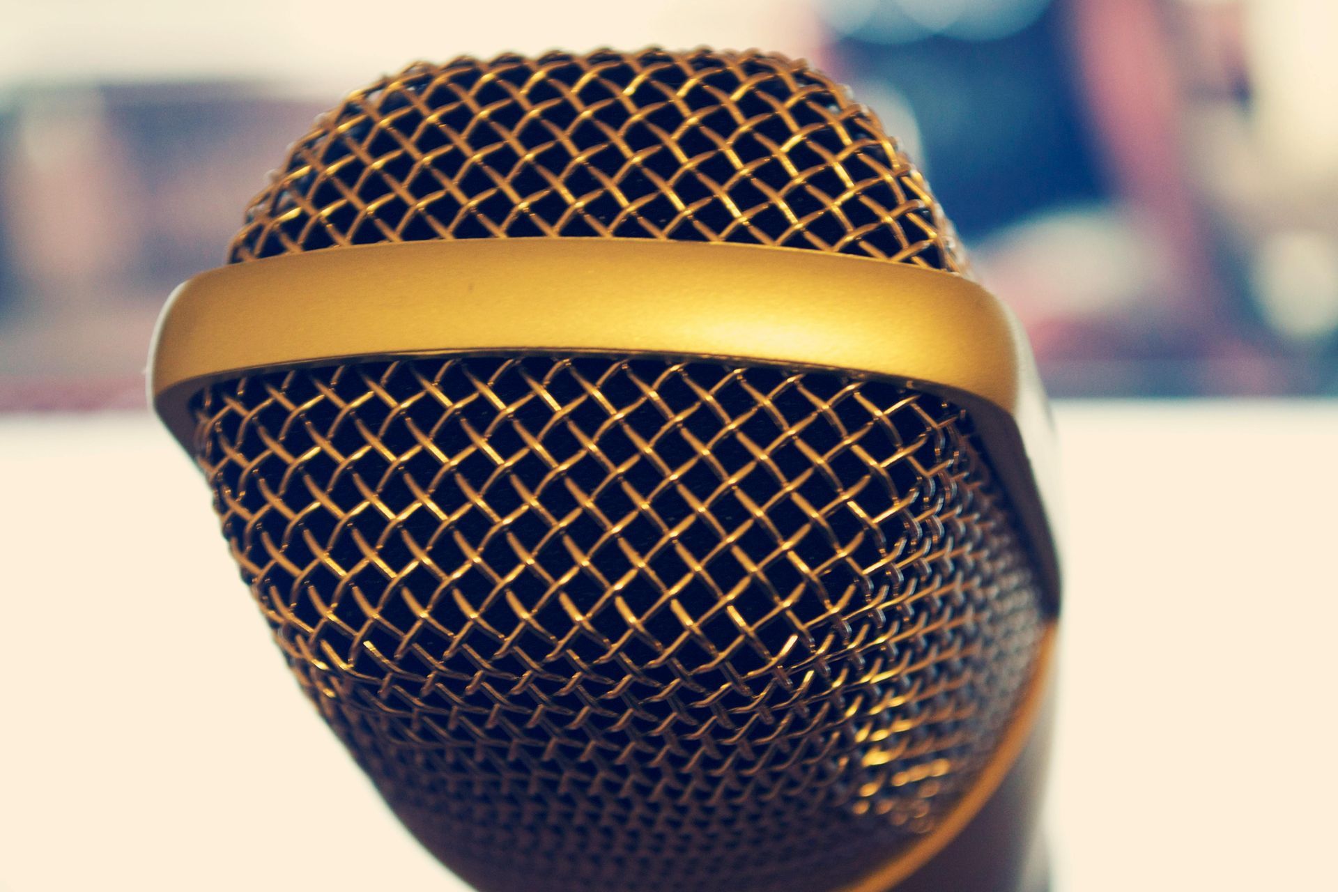 Gold microphone, close-up, with mesh grill. The microphone has a golden cap and a blurred background.