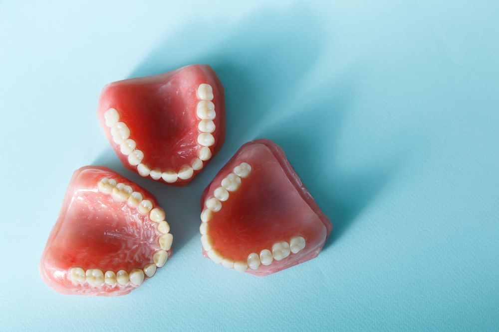 Three Dentures Are Sitting On Top Of Each Other On A Blue Surface — Dentures Direct Taree-Rod Hinton In Taree, NSW