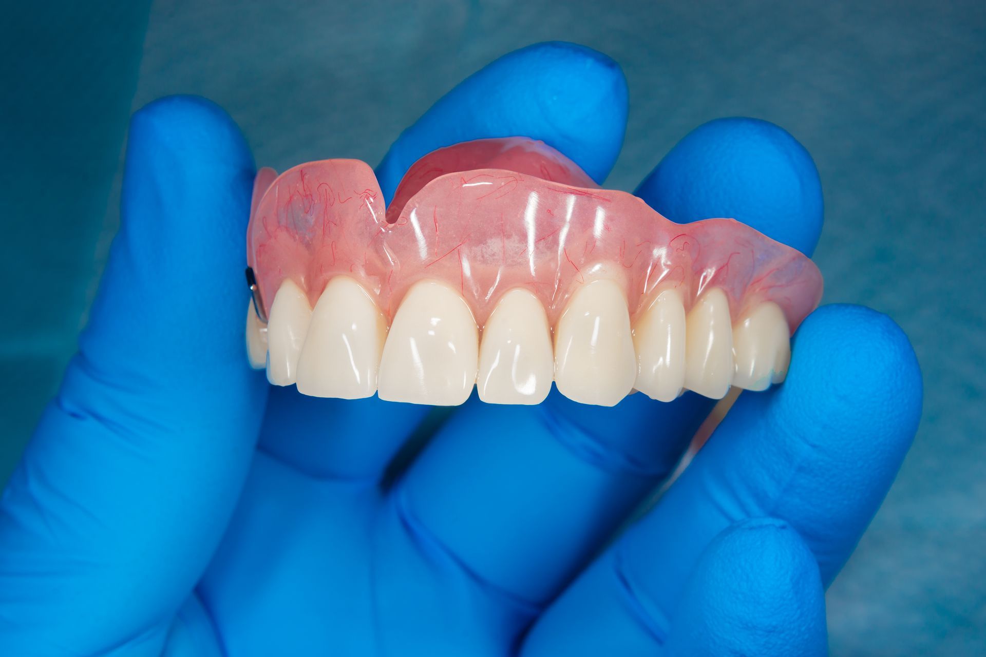 A Person Wearing Blue Gloves Is Holding A Denture In Their Hand — Dentures Direct Taree-Rod Hinton In Taree, NSW
