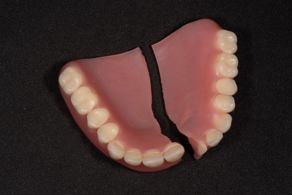 A Broken Denture Is Sitting On A Black Surface — Dentures Direct Taree-Rod Hinton In Taree, NSW