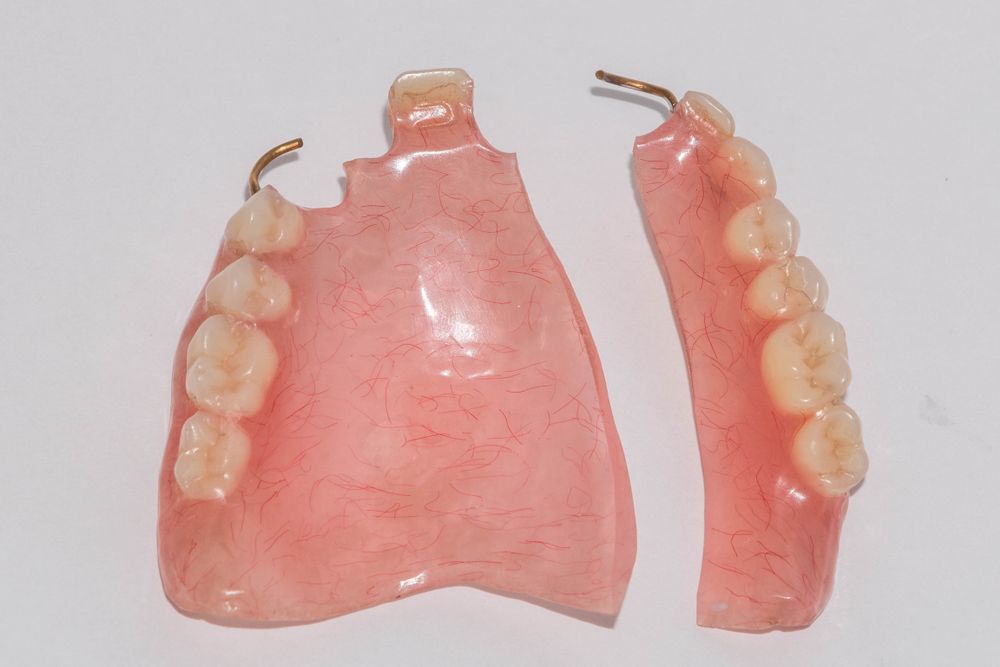 A Broken Denture Is Sitting On A White Surface — Dentures Direct Taree-Rod Hinton In Taree, NSW