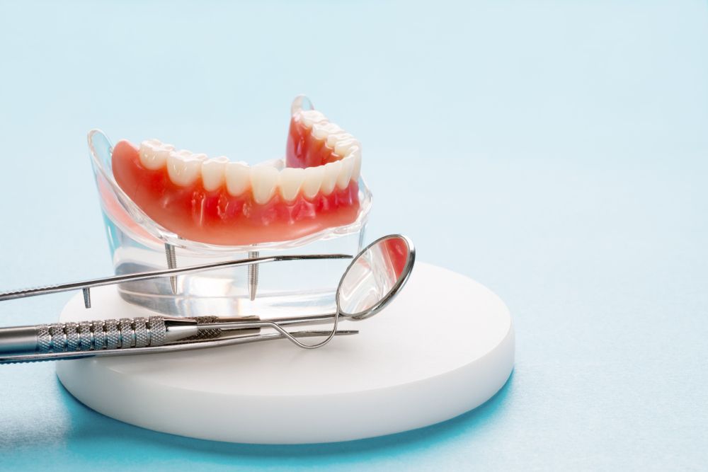 A Model Of A Denture With Dental Instruments On A Blue Background — Dentures Direct Taree-Rod Hinton In Taree, NSW