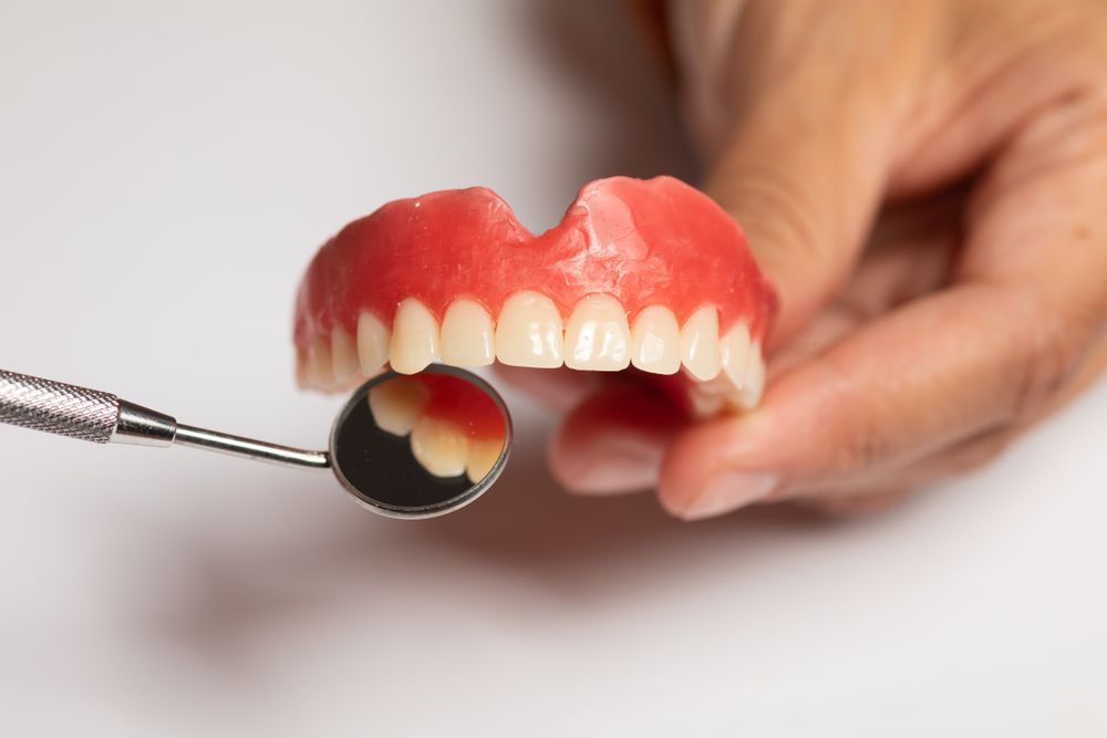 A Person Is Examining A Denture With A Dental Mirror — Dentures Direct Taree-Rod Hinton In Taree, NSW