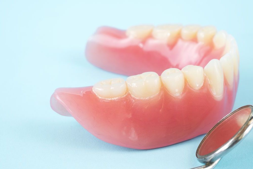 A Close Up Of A Denture And A Dental Mirror On A Blue Background — Dentures Direct Taree-Rod Hinton In Taree, NSW