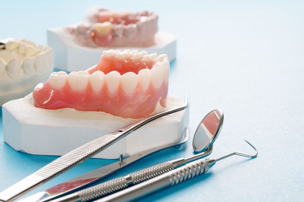 A Pair Of Dentures And Dental Instruments On A Blue Surface — Dentures Direct Taree-Rod Hinton In Taree, NSW