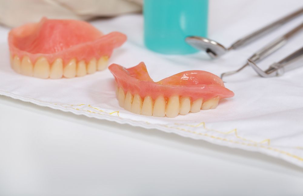 A Pair Of Dentures Sitting On Top Of A White Cloth Next To Dental Instruments — Dentures Direct Taree-Rod Hinton In Taree, NSW