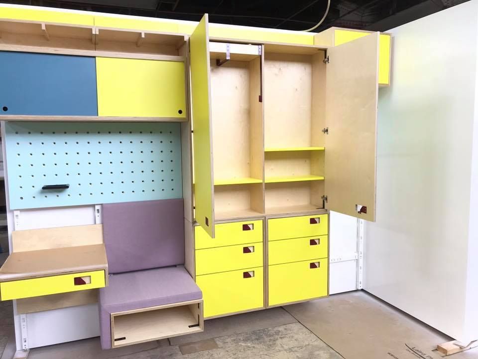 A modular, colorful closet system with open doors, drawers, and a small desk. Yellow, blue, and lavender hues.