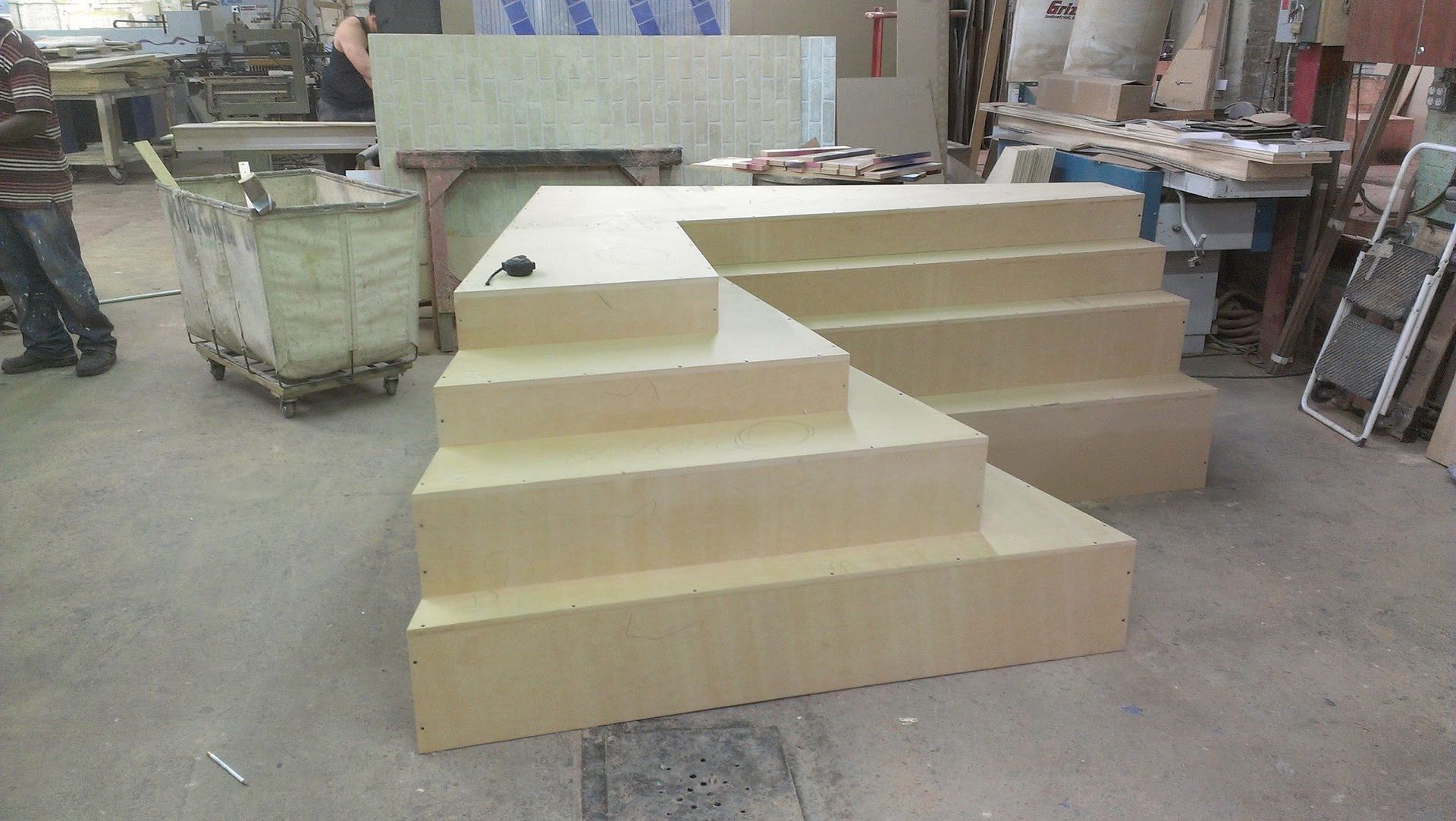 A wooden, light-brown stepped platform and stairs, possibly for a stage, in a workshop.