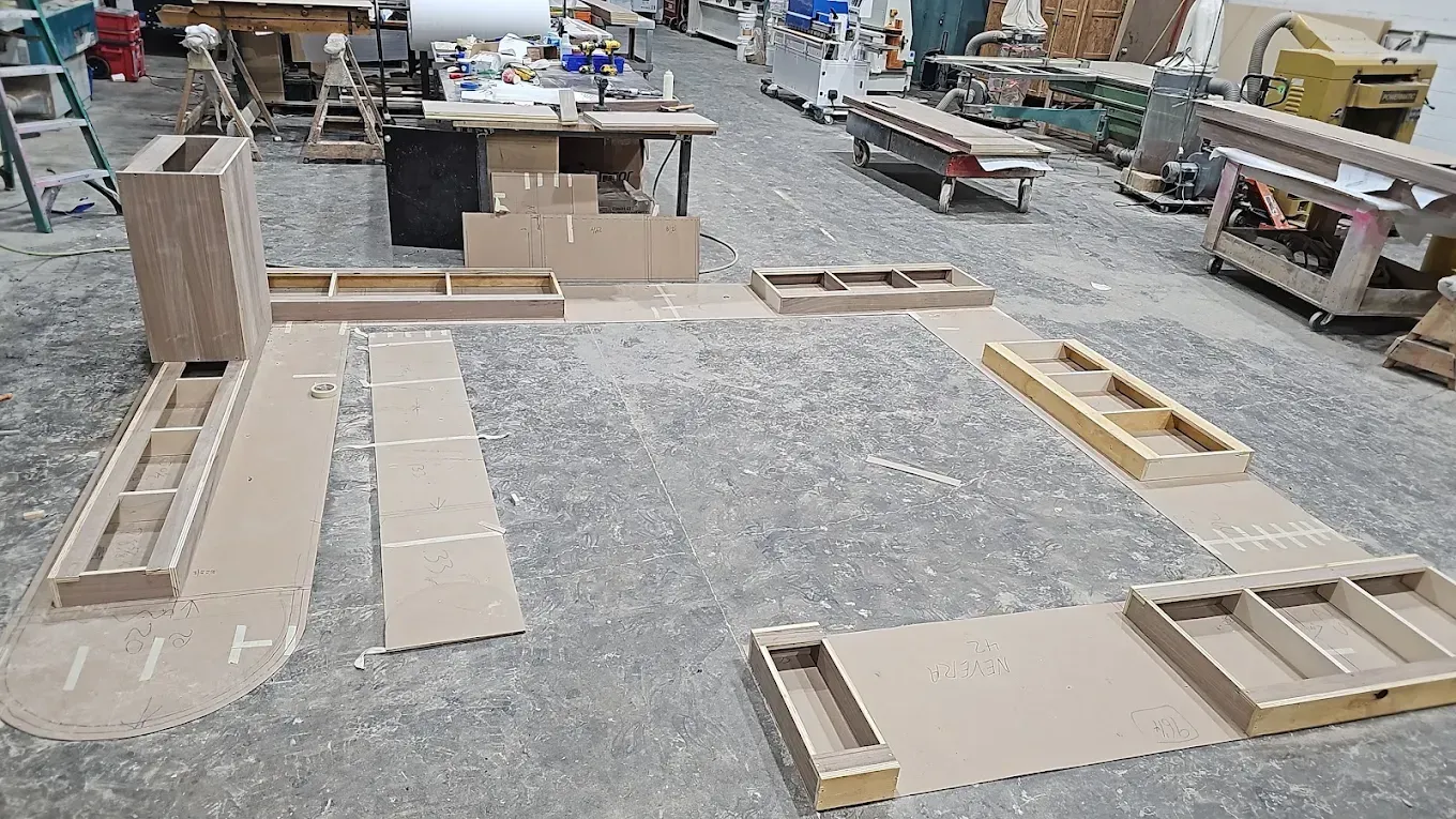 Cardboard furniture mockups laid out on a gray workshop floor, alongside wood construction pieces.