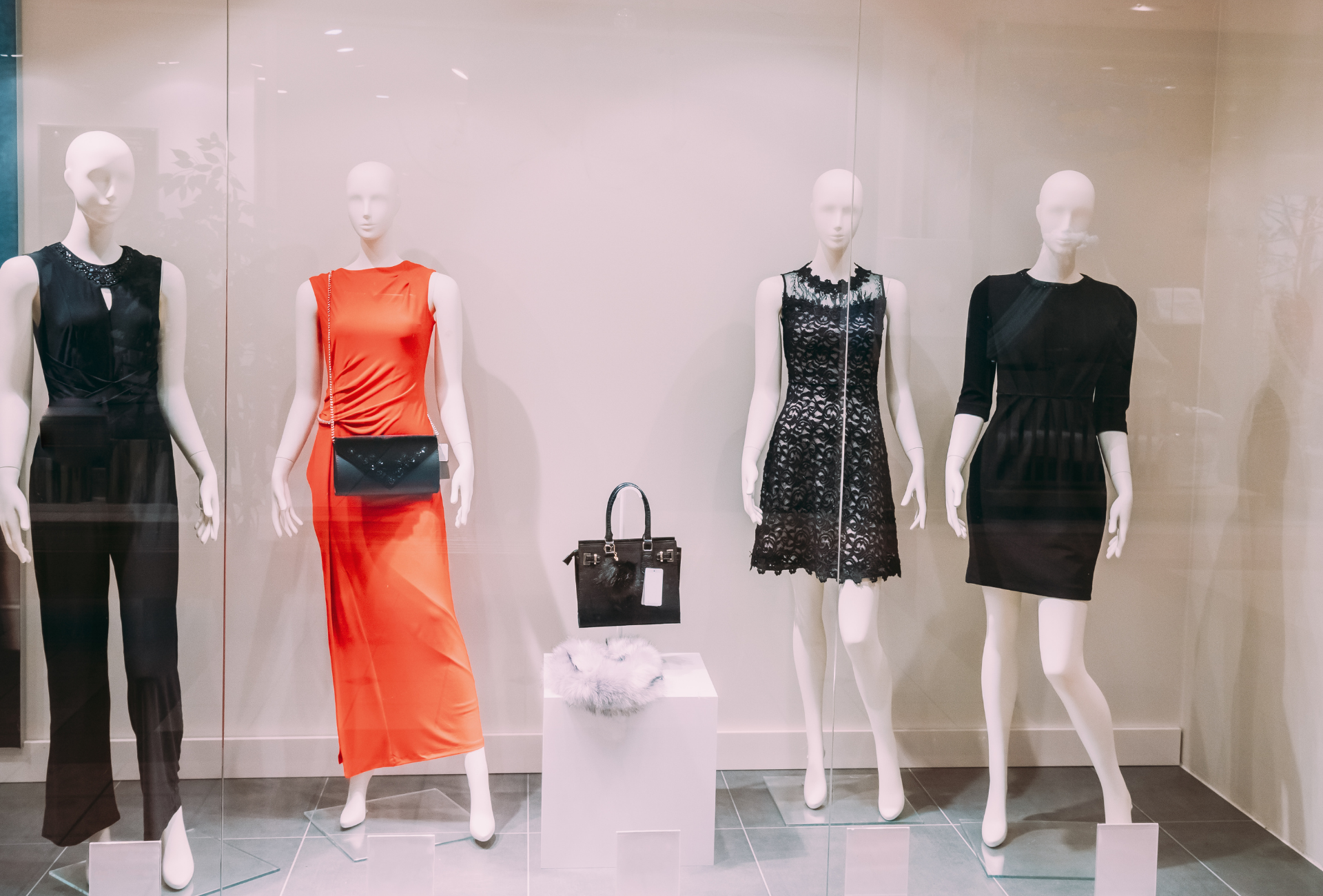 Four mannequins wearing women's clothing in a store window display, including a red dress and black outfits.