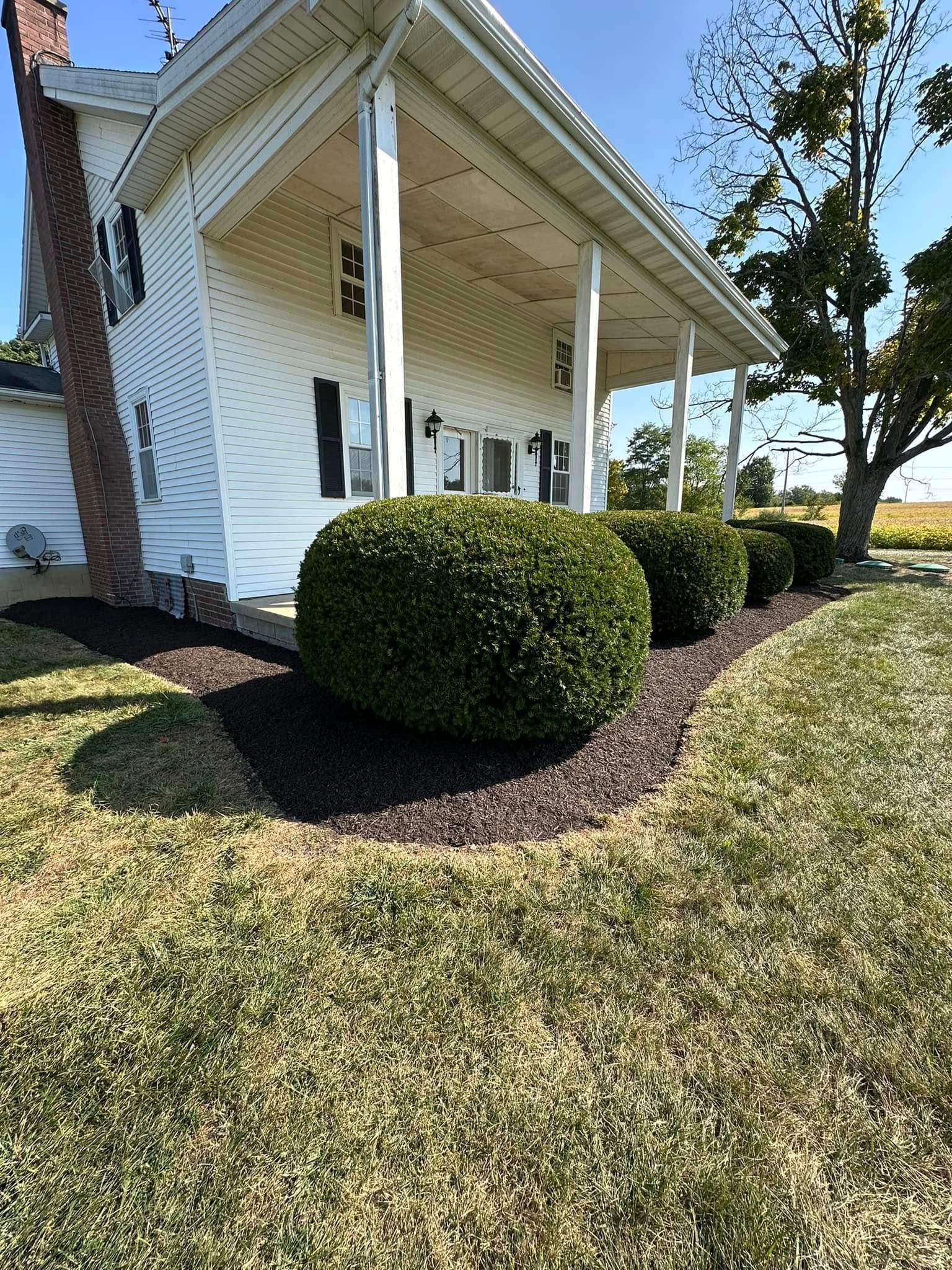 White house porch with white columns, trimmed green shrubs, and a sunlit lawn.