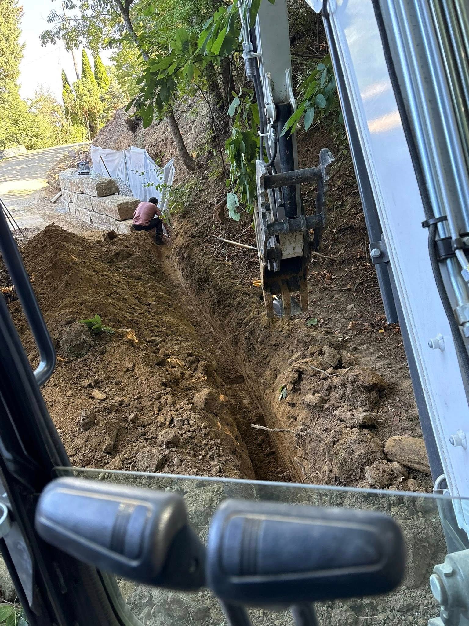 Excavator cab overlooking a muddy dirt slope beside a fence and trees