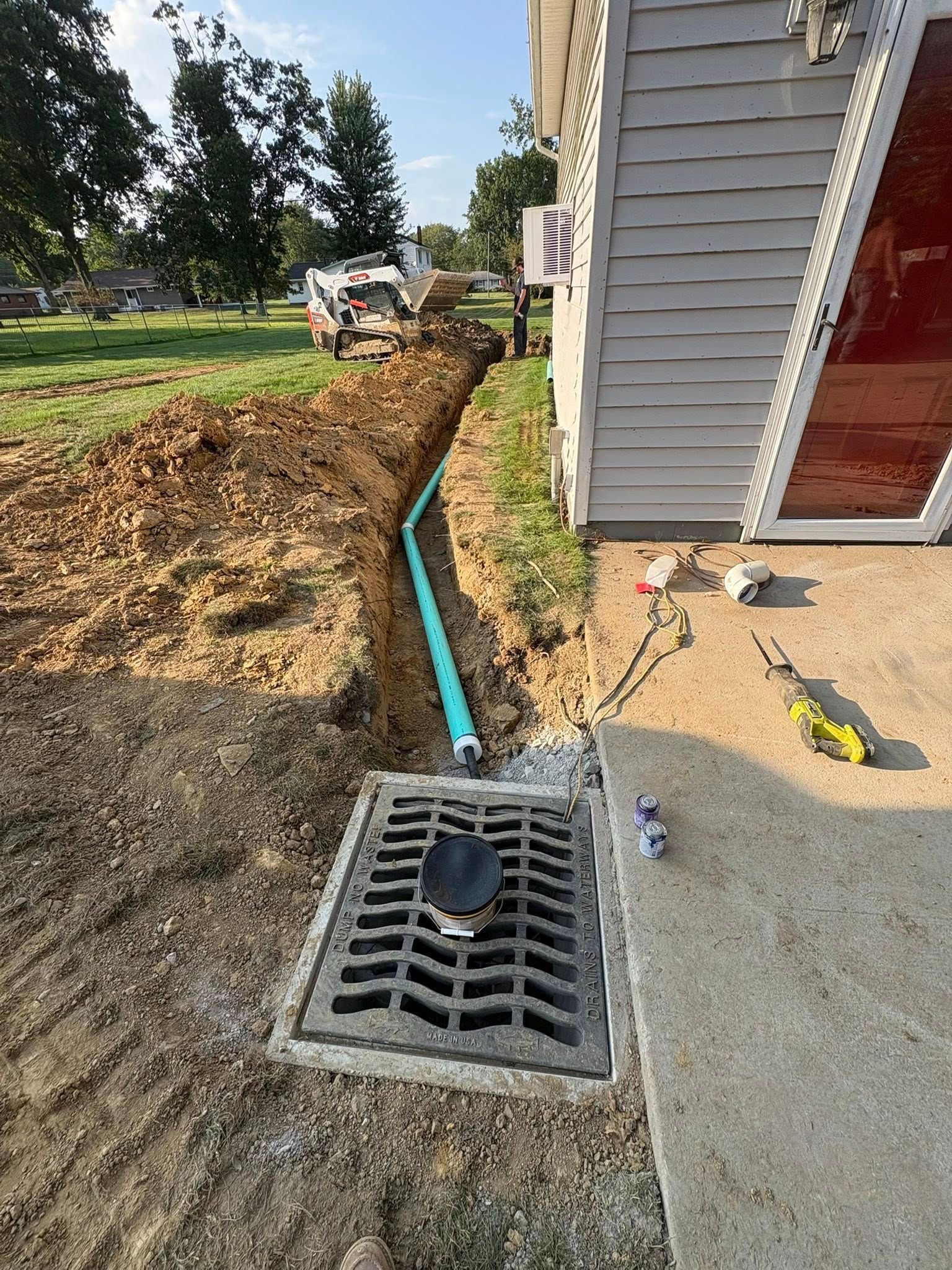 Excavation beside house foundation with blue pipe and drain grate in the foreground