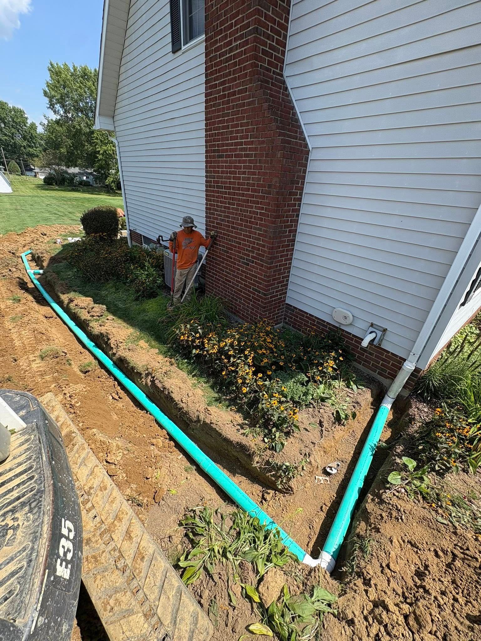 Garden bed by a brick house with turquoise edging along the foundation and a small sprinkler/pipe fixture.