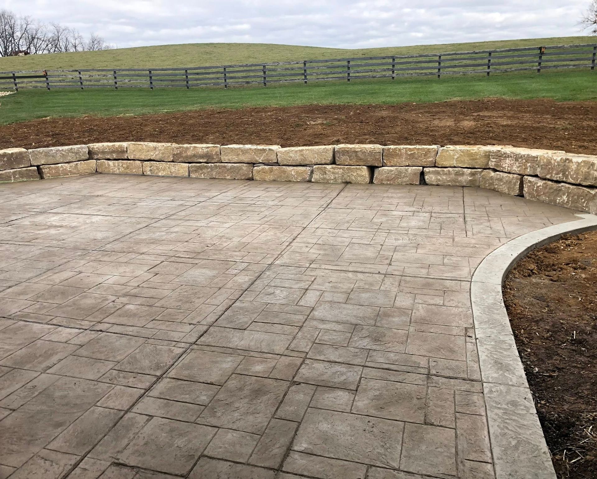 Stone patio with a curved retaining wall in a grassy outdoor landscape