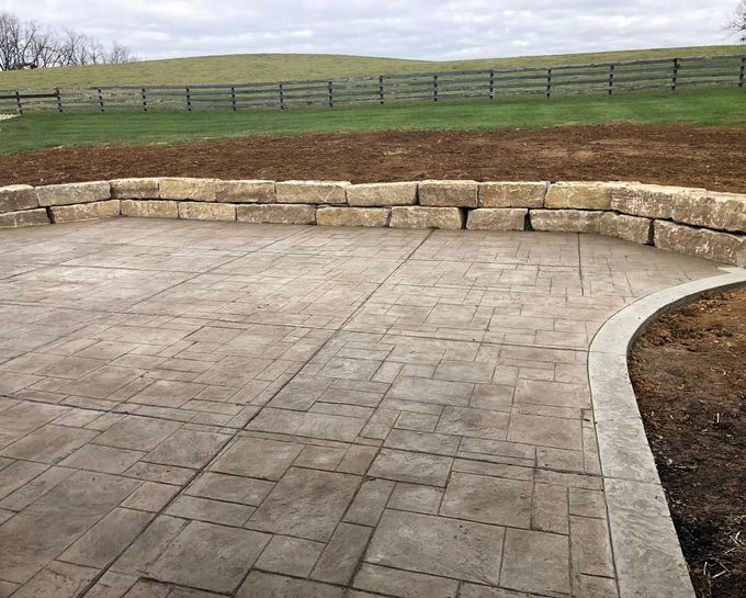Stone patio with curved retaining wall overlooking a grassy hillside and wooden fence