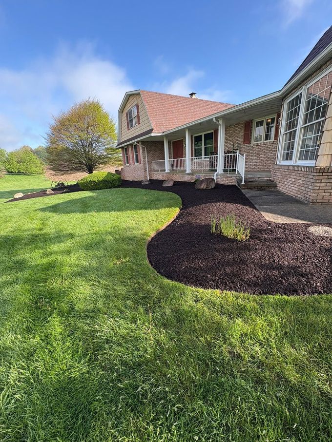 Brick house with covered porch, green lawn, and landscaped mulch beds under a clear blue sky