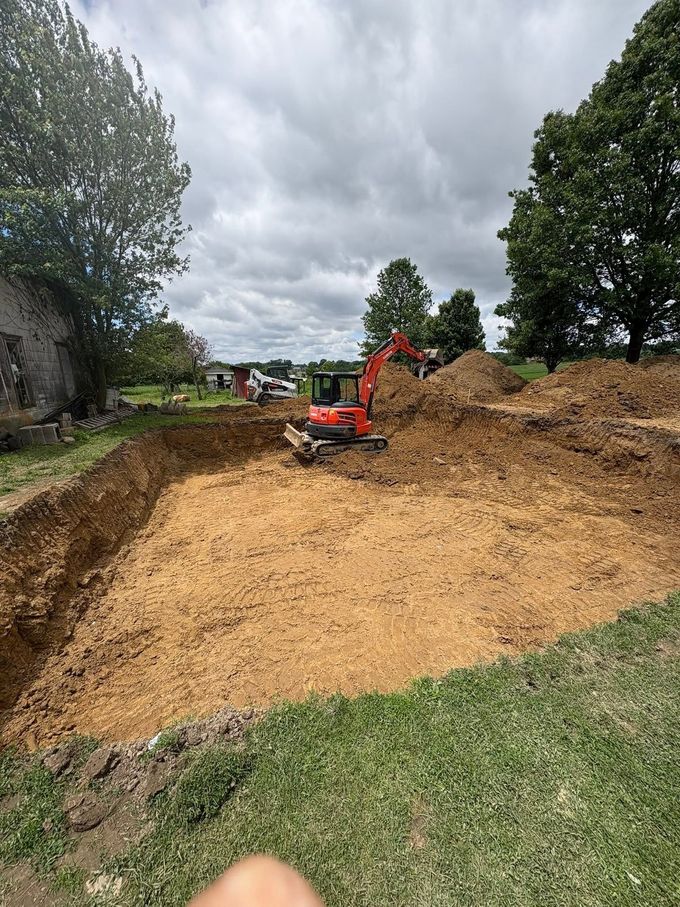 Orange excavator clearing a dirt embankment on a cloudy construction site with trees nearby