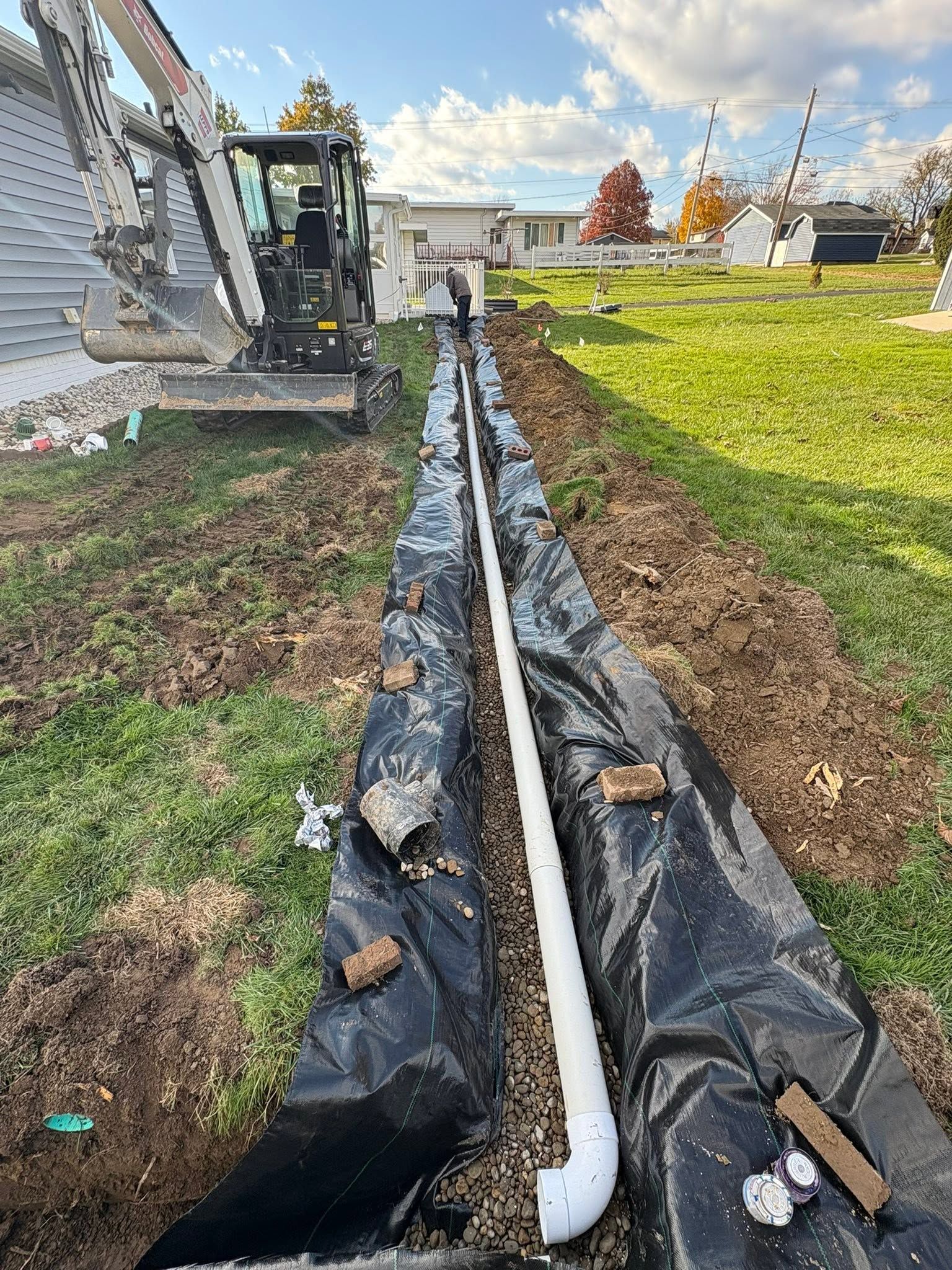 Black drainage fabric trench beside a house, with a white pipe running through a grassy yard.