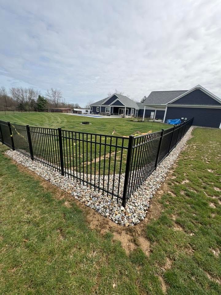 Black metal fence around a gravel yard beside a gray house and garage under a cloudy sky