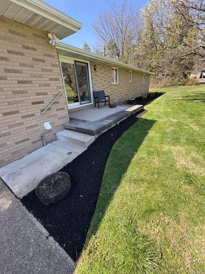 Back patio with concrete steps, small deck, sliding glass door, and grassy yard beside a brick house