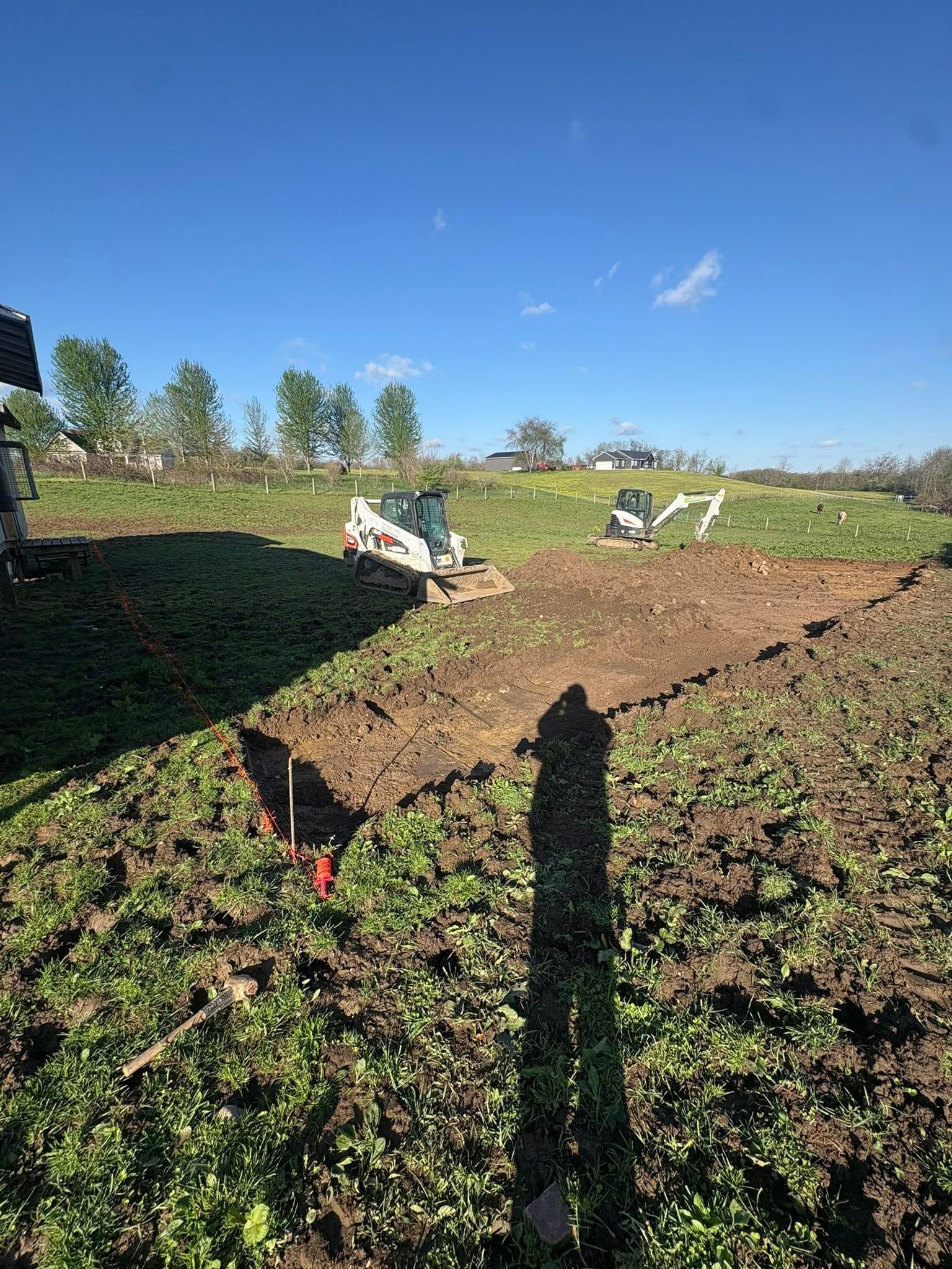 People digging in a brown dirt field with white vehicles under a blue sky, trees in the background