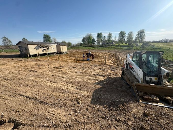 Construction site with excavator in a dirt field and workers near a trailer under a clear sky