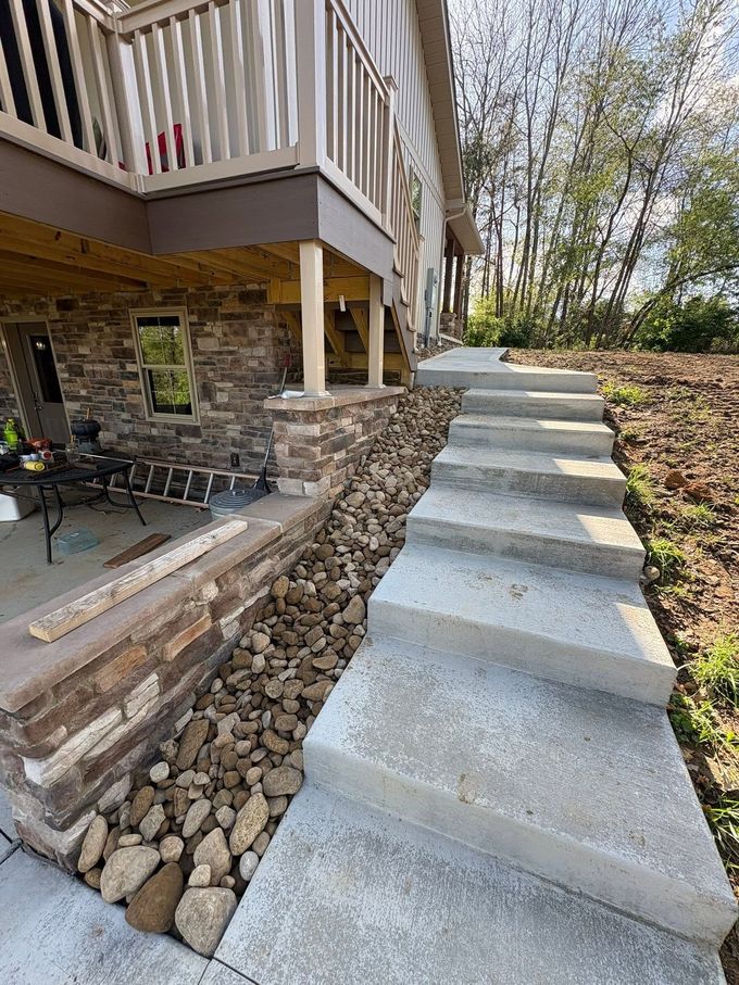 Concrete steps climbing beside a house with a stone retaining wall and deck above