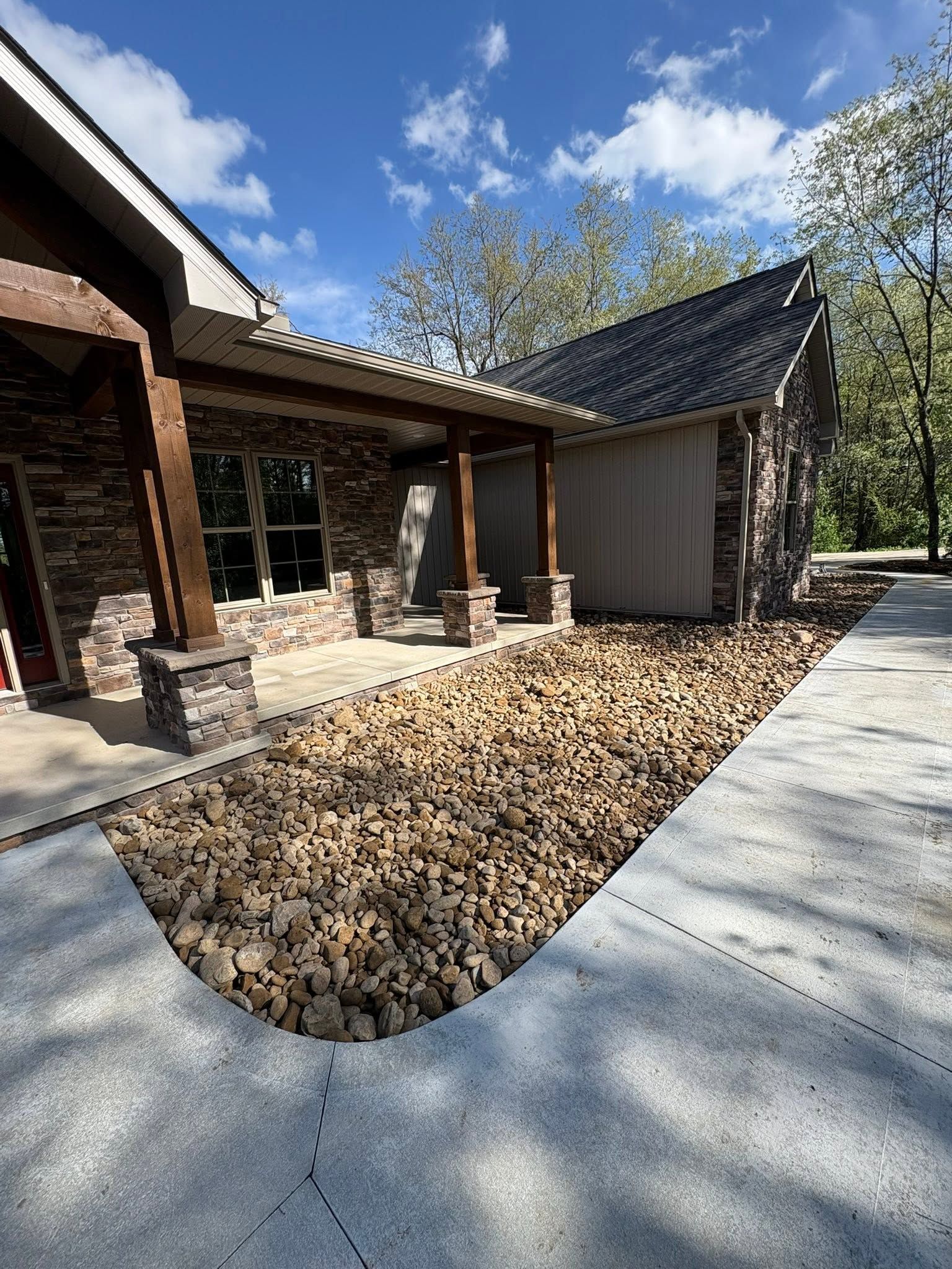Modern house patio with stone walkway, covered entry, and landscaped yard under a blue sky