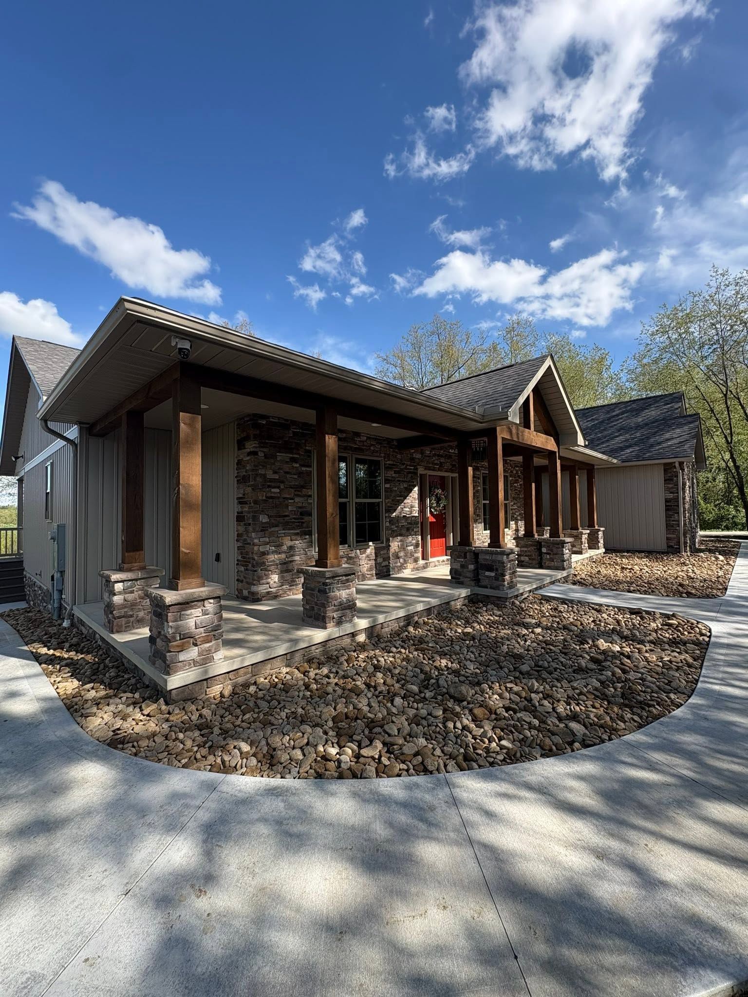 Modern rustic house with stone and wood exterior, front porch, and blue sky with clouds