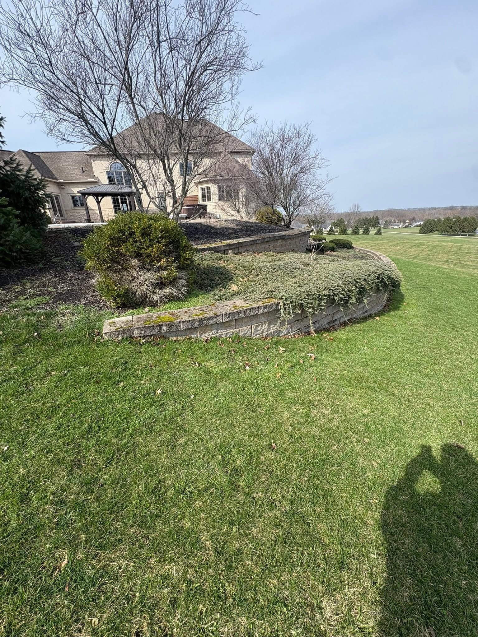 Stone house with a circular stone garden bed and leafless tree in a sunny grassy field