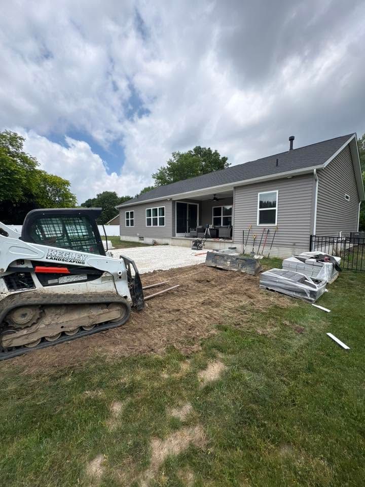 House under construction with a bobcat skid steer, fresh concrete patio, and siding work in progress