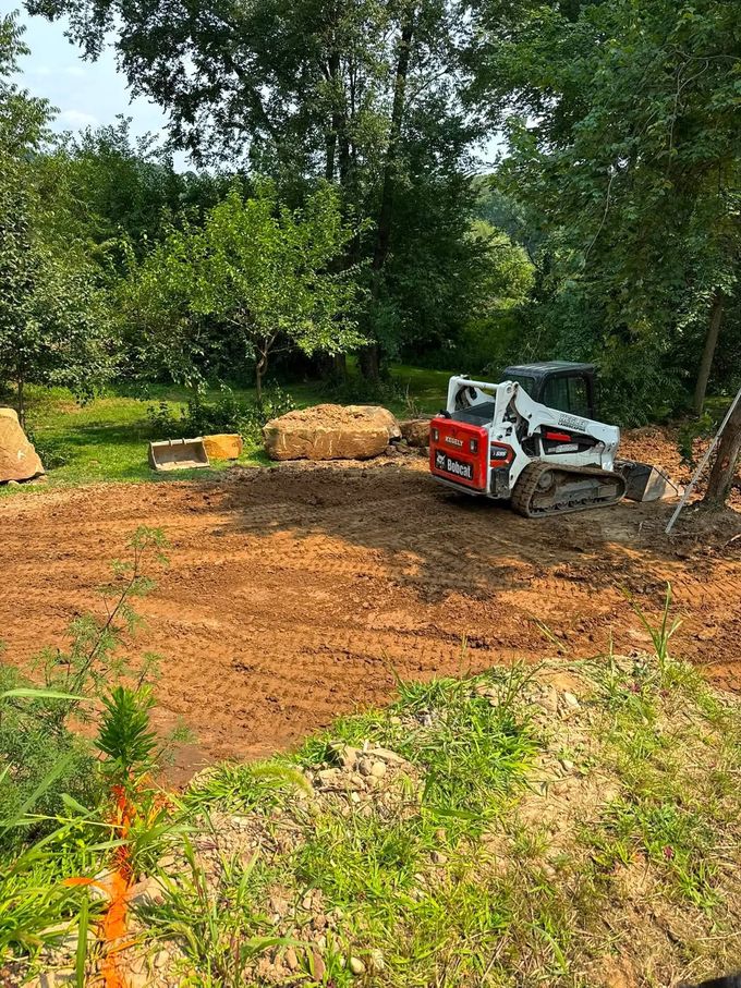 Compact track loader grading dirt in a wooded clearing with hay bales nearby