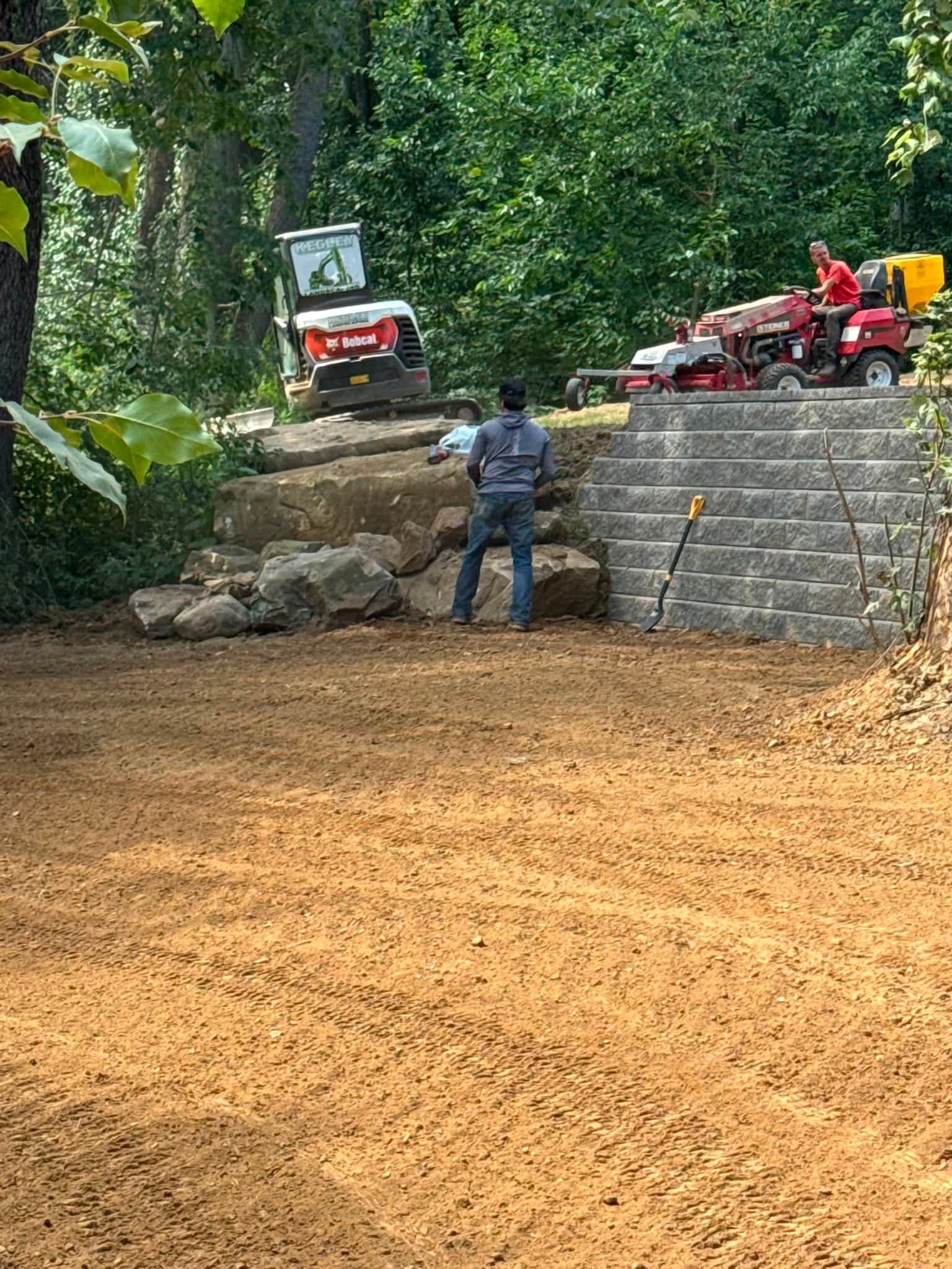 Worker standing before stone steps at a muddy construction site with a red truck and excavator on top.