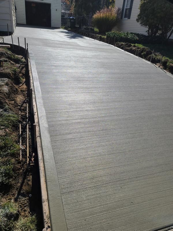 Wet concrete pouring from a truck chute onto a construction site, forming a gravelly slab surface
