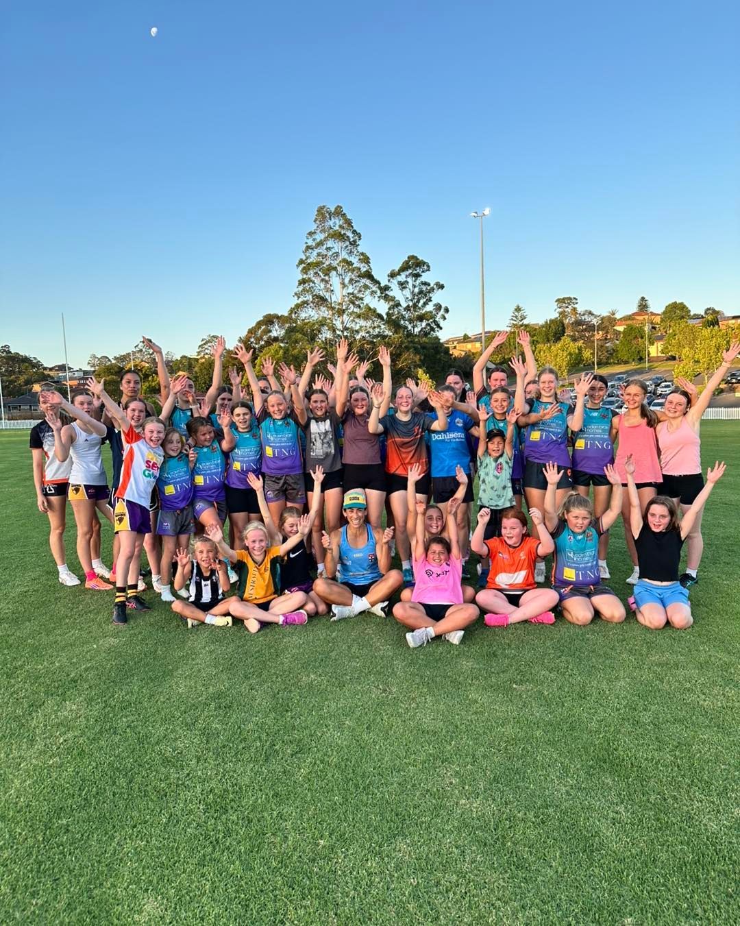 Group of people on a green field with arms raised in the air.  They are wearing athletic clothing.