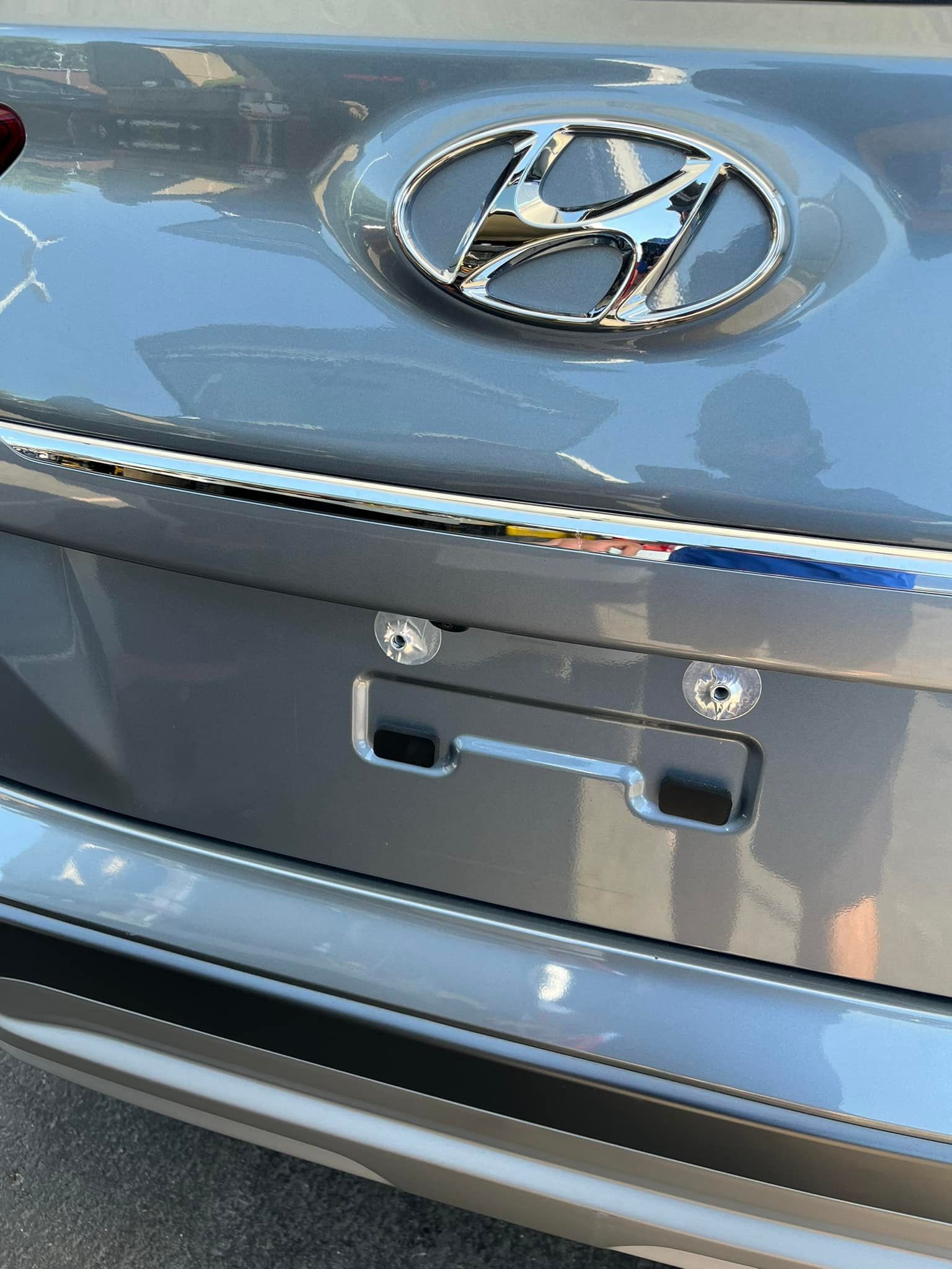 A close-up of a gray Hyundai car trunk, showing the metallic logo and the empty mounting area for a license plate.