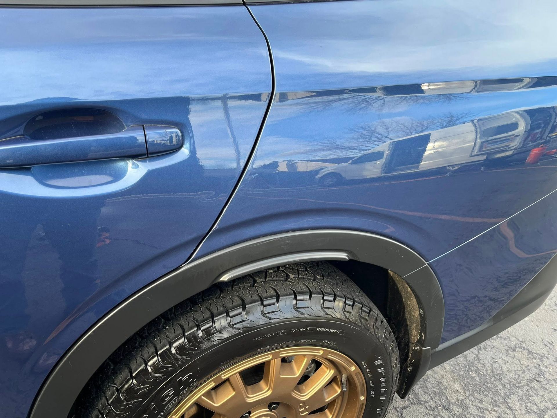 A blue car rear panel and door with a black plastic wheel arch trim and a bronze-colored wheel.