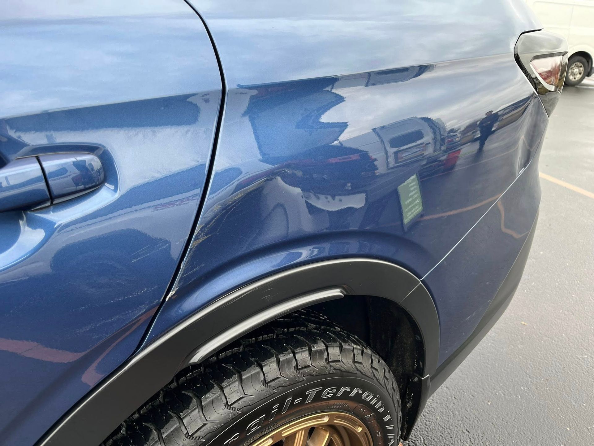 A close-up view of the rear side panel, wheel arch, and tire of a metallic blue vehicle parked outdoors.