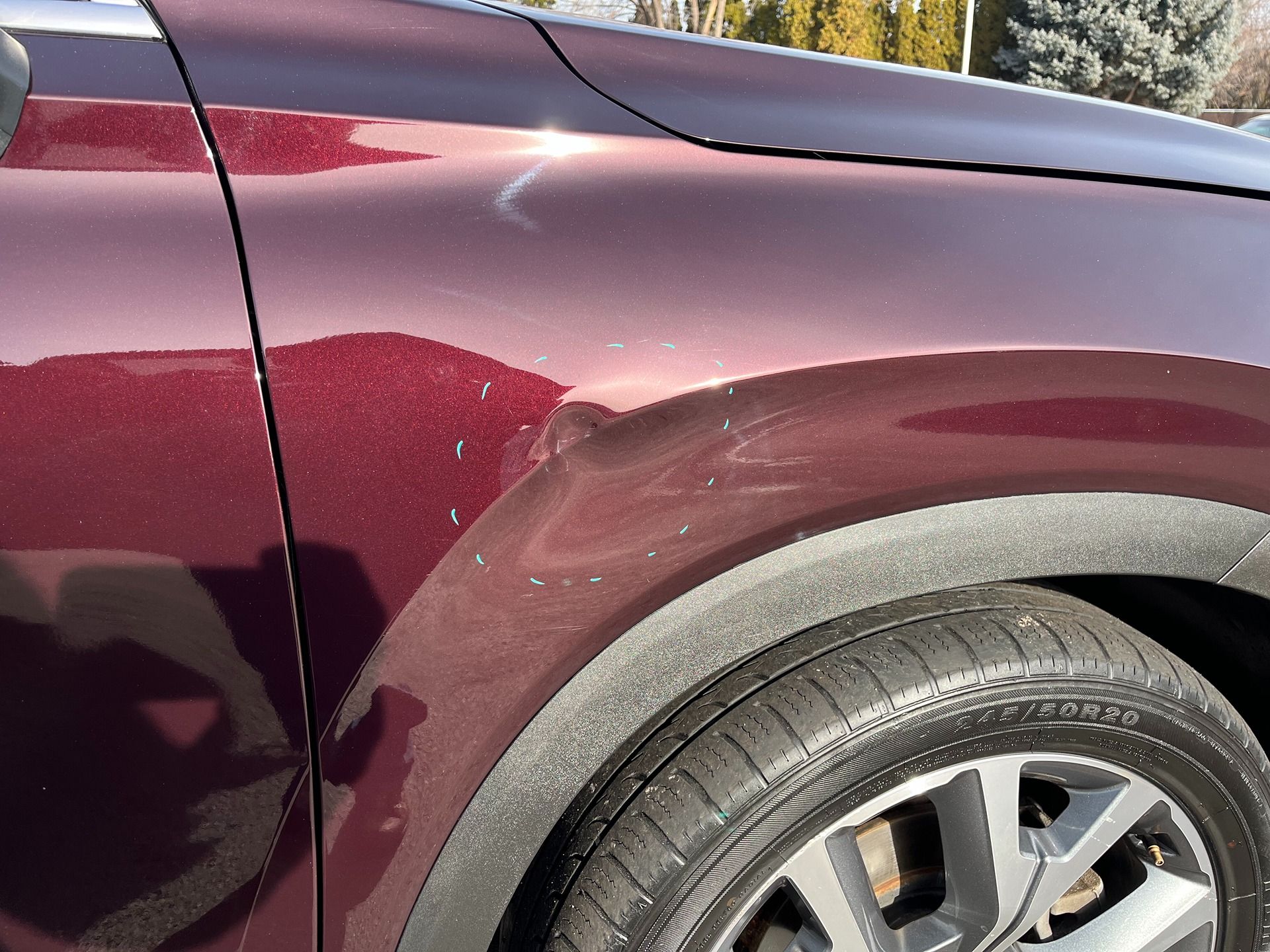 A maroon car fender showing a noticeable dent and surface scratches above the front wheel arch.