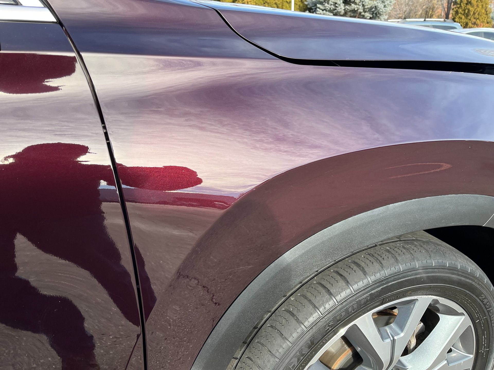 A close-up view of the front quarter panel and wheel arch of a maroon car with a person's reflection visible.