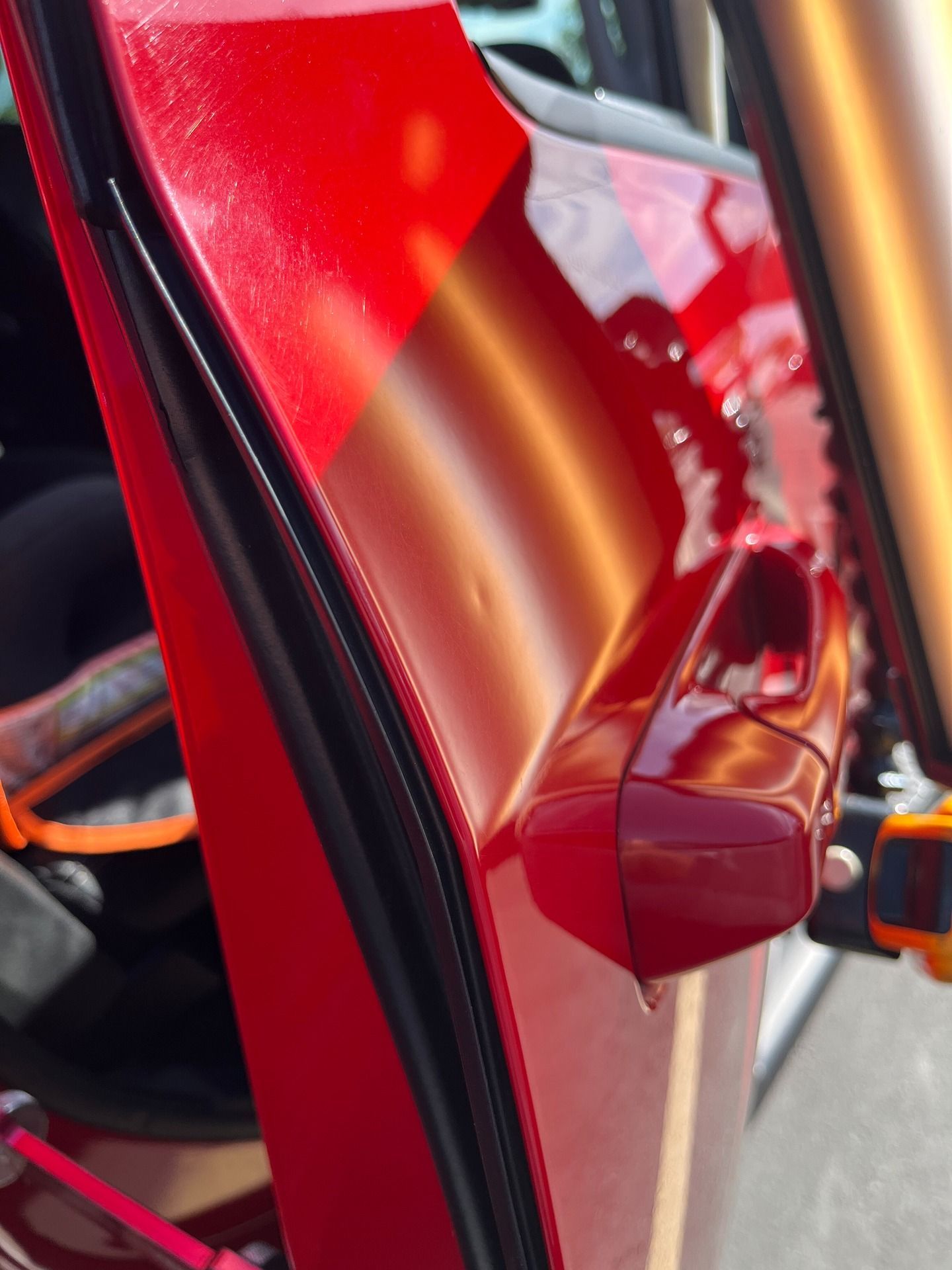 A close-up of a bright red car door panel featuring a small, shallow dent near the door handle.
