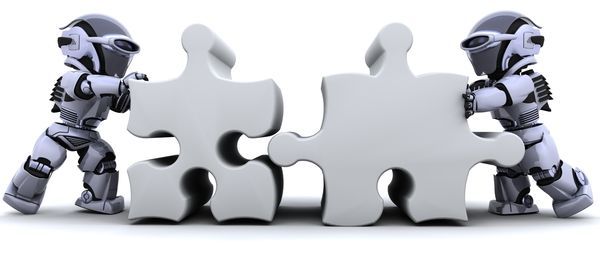 Zwei Spielzeugroboter, die übergrosse graue Puzzleteile aneinander schieben.