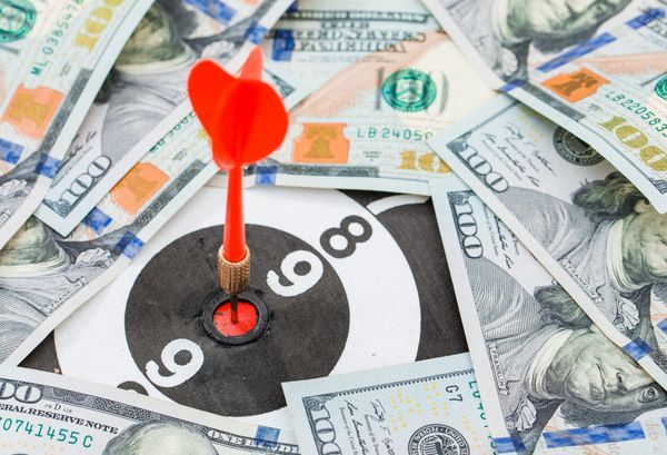 Ein roter Dartpfeil im Bullseye der Zielscheibe, umgeben von verstreuten US-Dollar-Scheinen.
