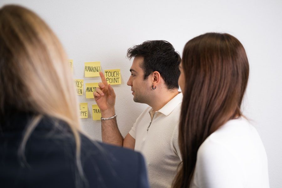 Eine Gruppe von Leuten sieht sich Haftnotizen auf einer weissen Wand an.
