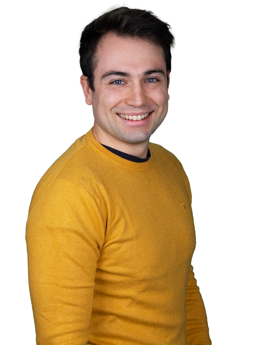 Ein Mann in einem gelbem Pullover lächelt in die Kamera.