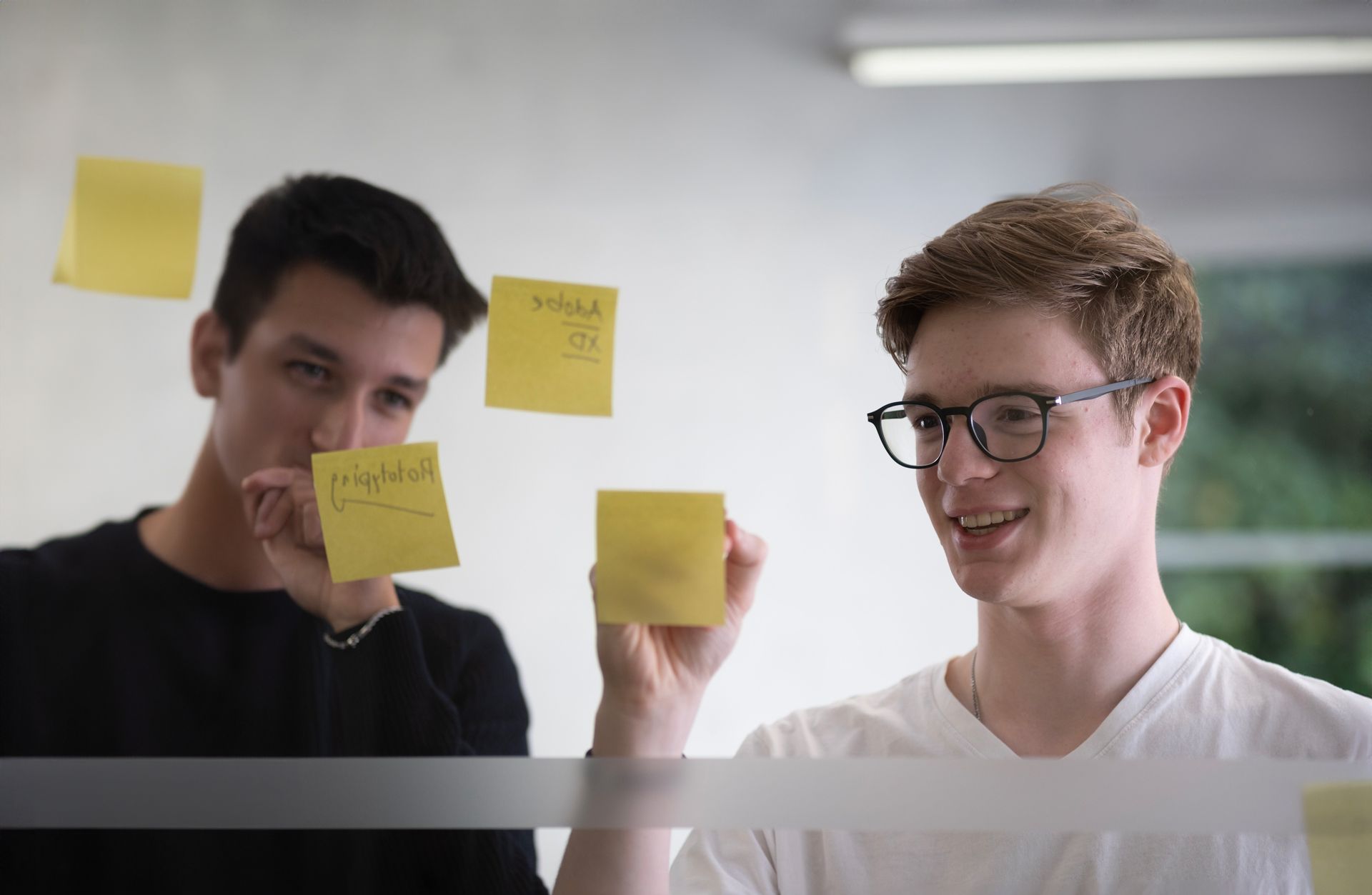 Zwei Personen stehen vor einer Glaswand und schreiben auf Post-its